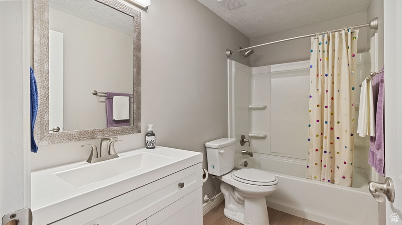 Full bathroom featuring shower / bath combo with shower curtain, visible vents, vanity, wood finished floors, and toilet