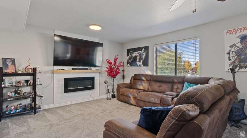 Carpeted living room with a glass covered fireplace, baseboards, and ceiling fan