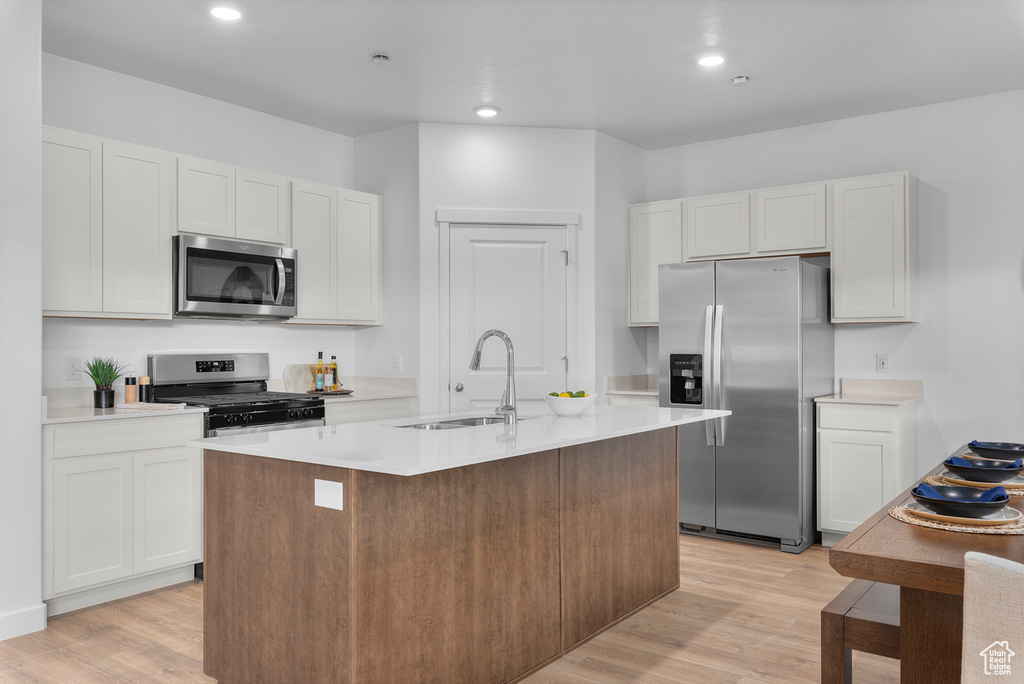 Kitchen featuring light wood-type flooring, a sink, light countertops, stainless steel appliances, and an island with sink