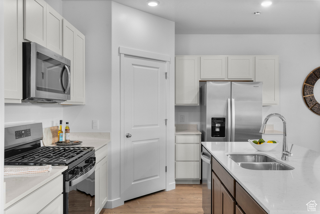 Kitchen with a sink, appliances with stainless steel finishes, white cabinets, and light wood-style floors