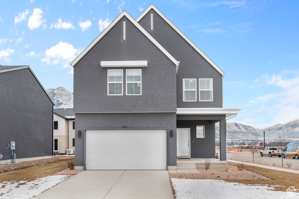 View of front of property with a porch, driveway, a mountain view, an attached garage, and stucco siding