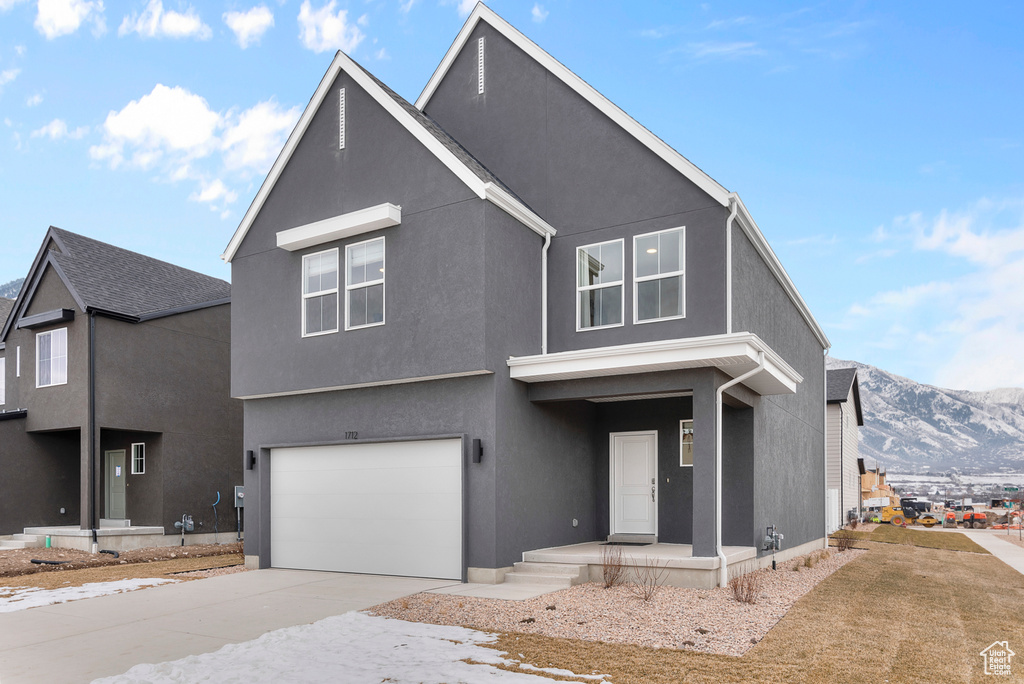 View of front of property featuring an attached garage, stucco siding, a mountain view, covered porch, and driveway