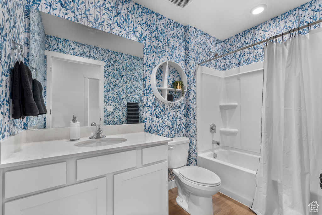 Full bath with vanity, wood finished floors, shower / bath combo, and wallpapered walls