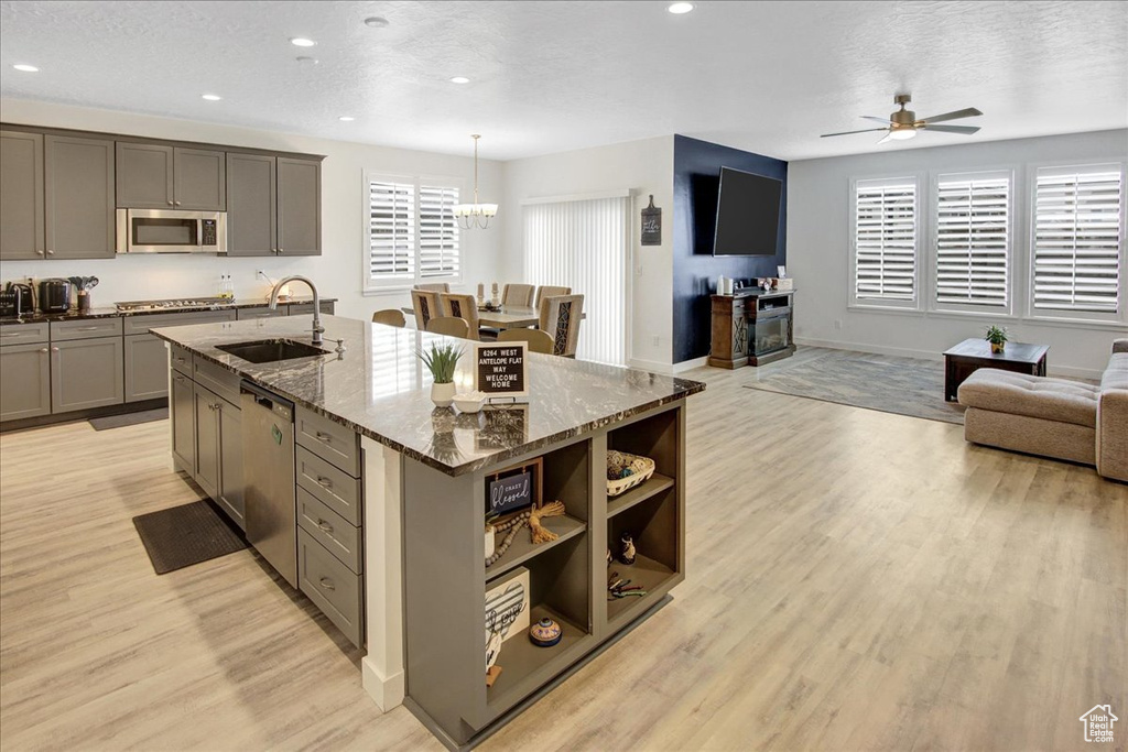Kitchen with ceiling fan with notable chandelier, open floor plan, a sink, appliances with stainless steel finishes, and gray cabinetry