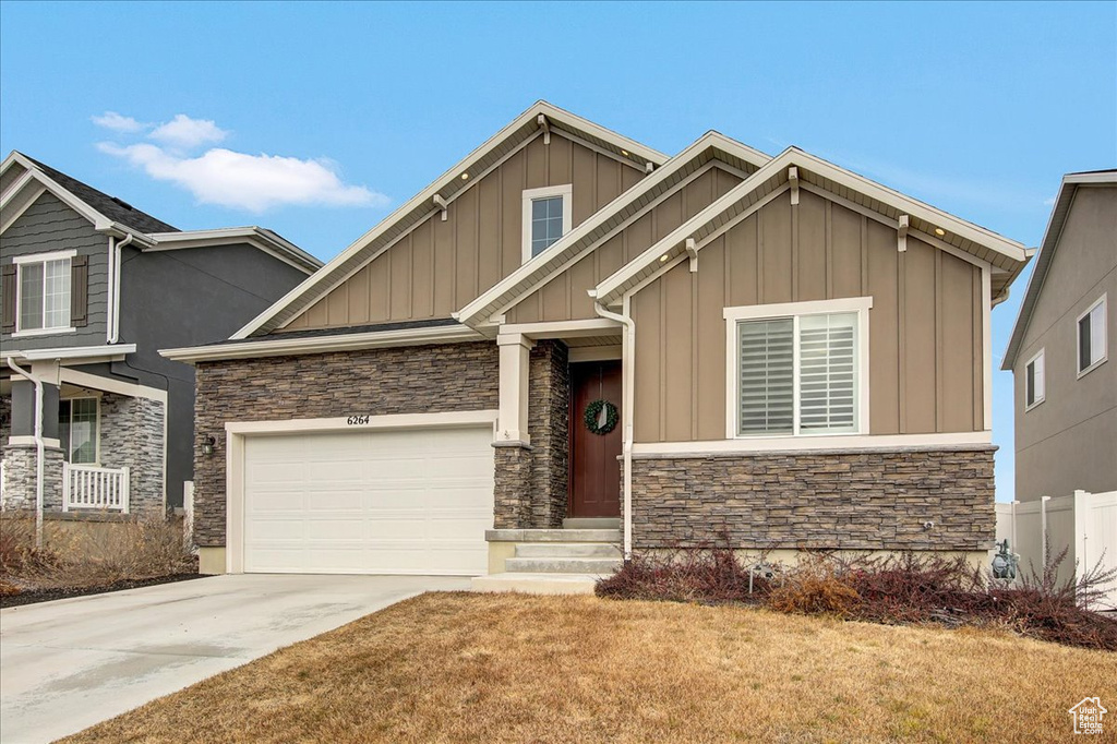 Craftsman-style home with an attached garage, stone siding, board and batten siding, a front yard, and concrete driveway