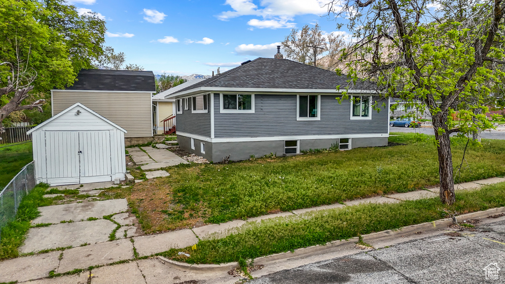 View of side of home featuring an outdoor structure, a yard, a shed, and roof with shingles