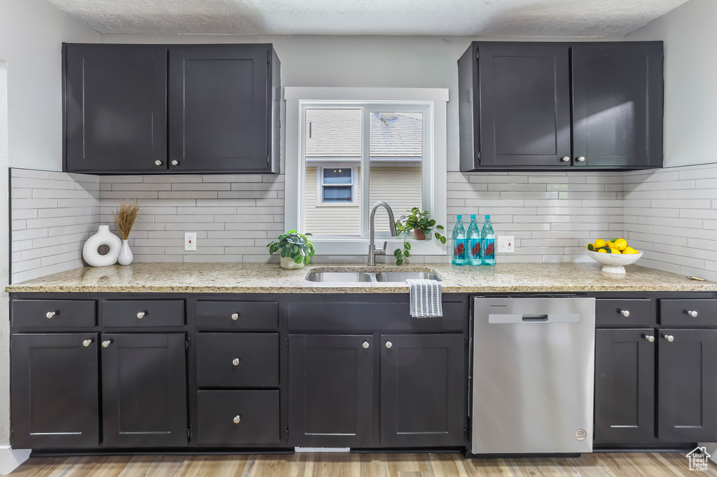 Kitchen with a sink, light stone countertops, backsplash, and dishwasher