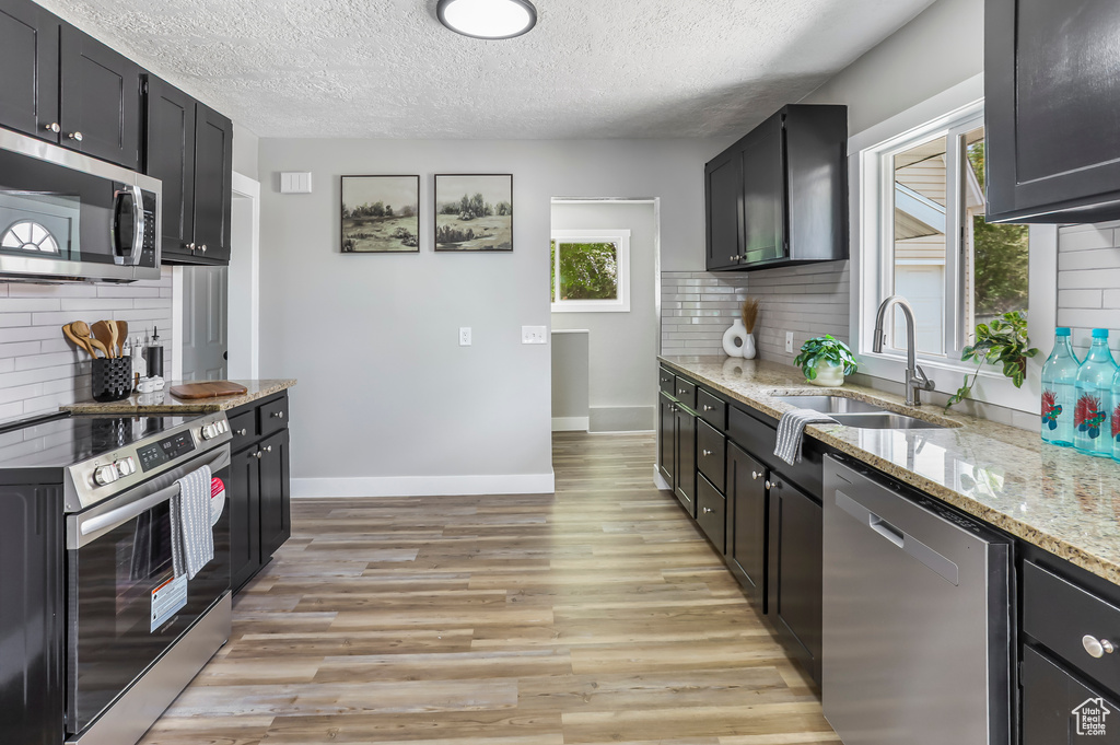 Kitchen featuring a sink, backsplash, light stone countertops, and stainless steel appliances