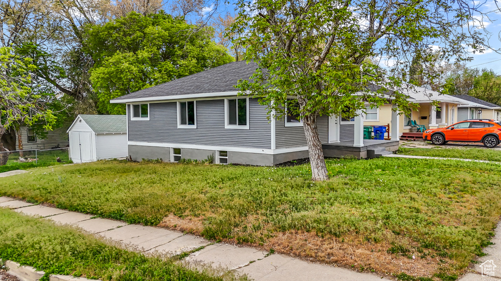 View of front of house with an outdoor structure, fence, a front yard, roof with shingles, and a shed