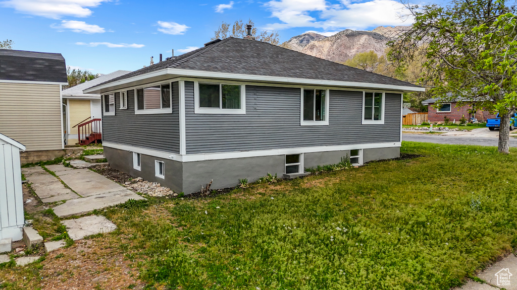 View of side of home featuring a lawn, roof with shingles, and a mountain view