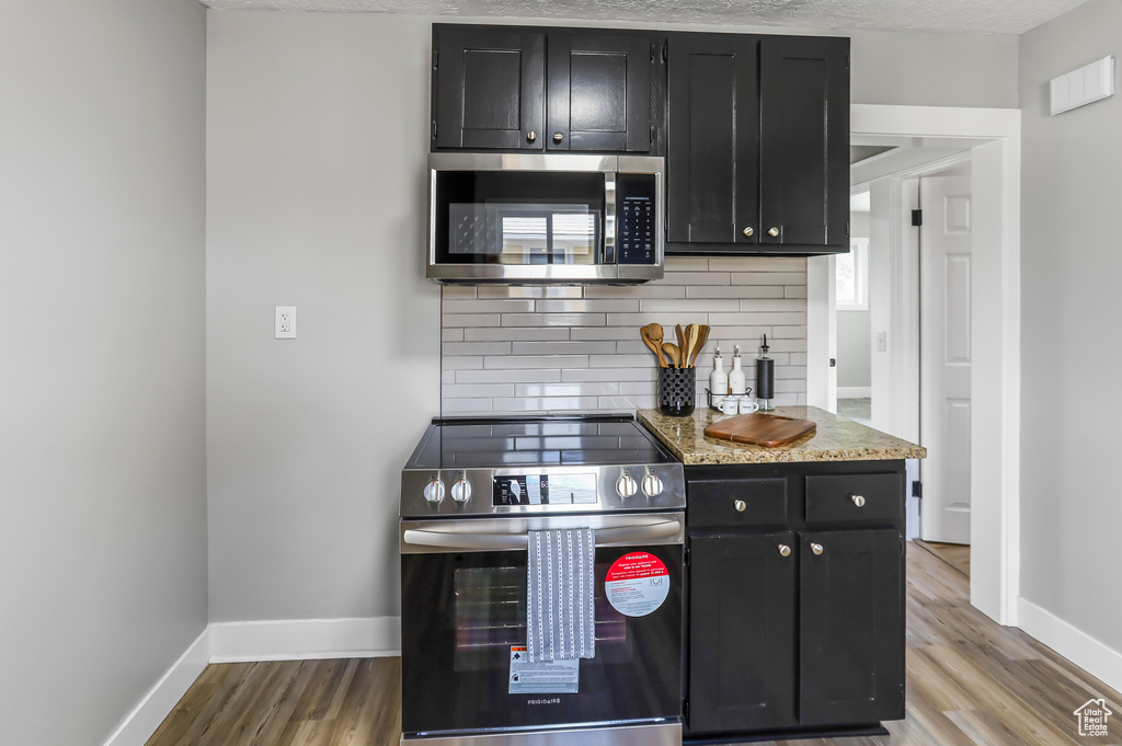 Kitchen with dark cabinetry, baseboards, appliances with stainless steel finishes, and tasteful backsplash