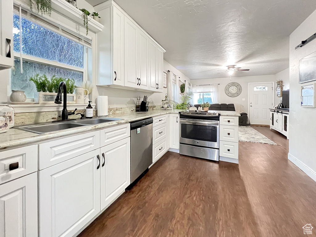 Kitchen with dark wood-style flooring, a sink, stainless steel appliances, a ceiling fan, and a peninsula