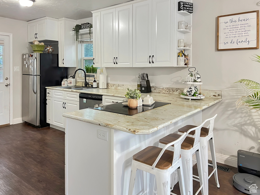 Kitchen featuring a sink, dishwashing machine, black electric stovetop, and white cabinetry