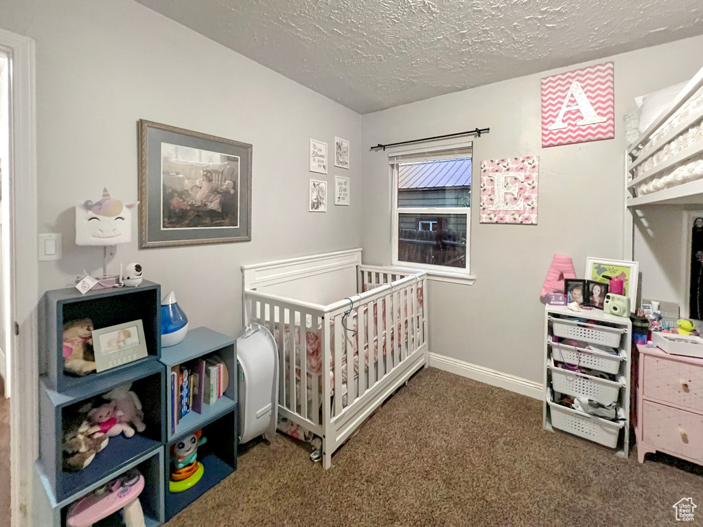 Bedroom featuring a crib, baseboards, carpet, and a textured ceiling