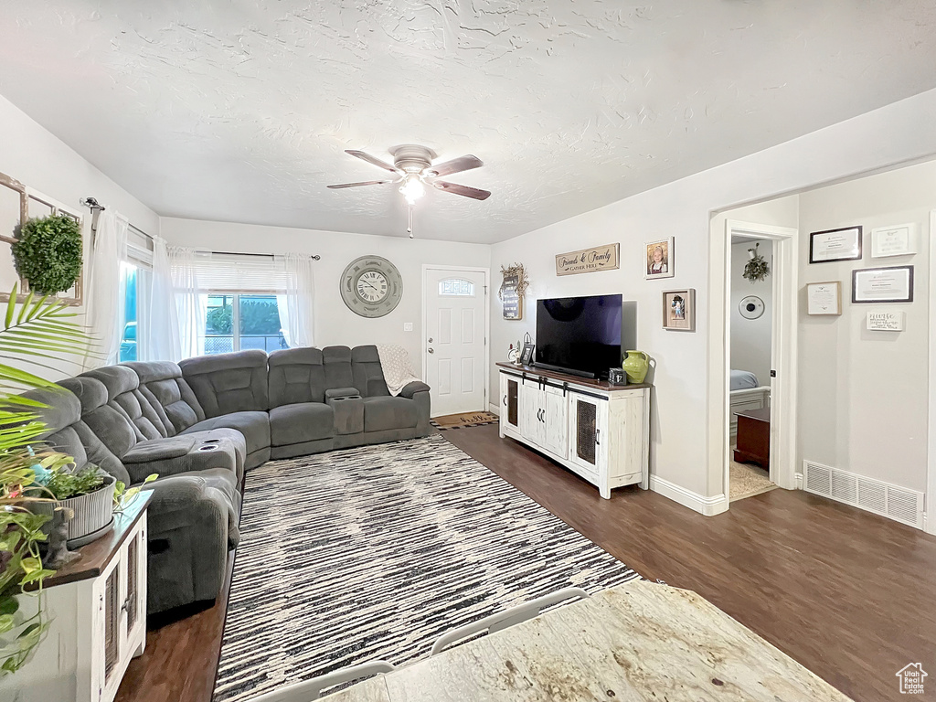 Living area with visible vents, baseboards, ceiling fan, dark wood-type flooring, and a textured ceiling