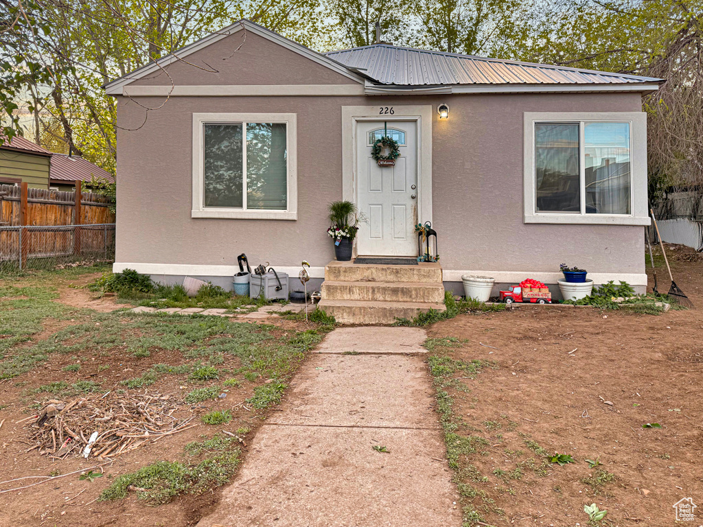 Bungalow-style home with stucco siding, fence, metal roof, and entry steps