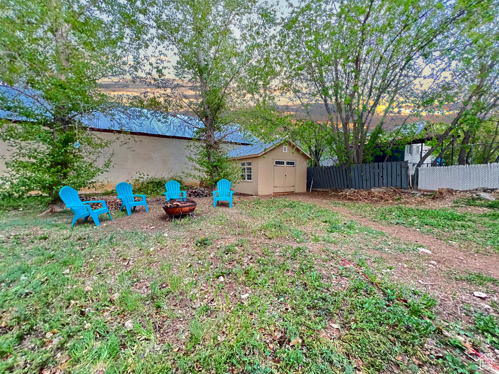 View of yard featuring an outdoor structure, a fire pit, fence, and a storage unit