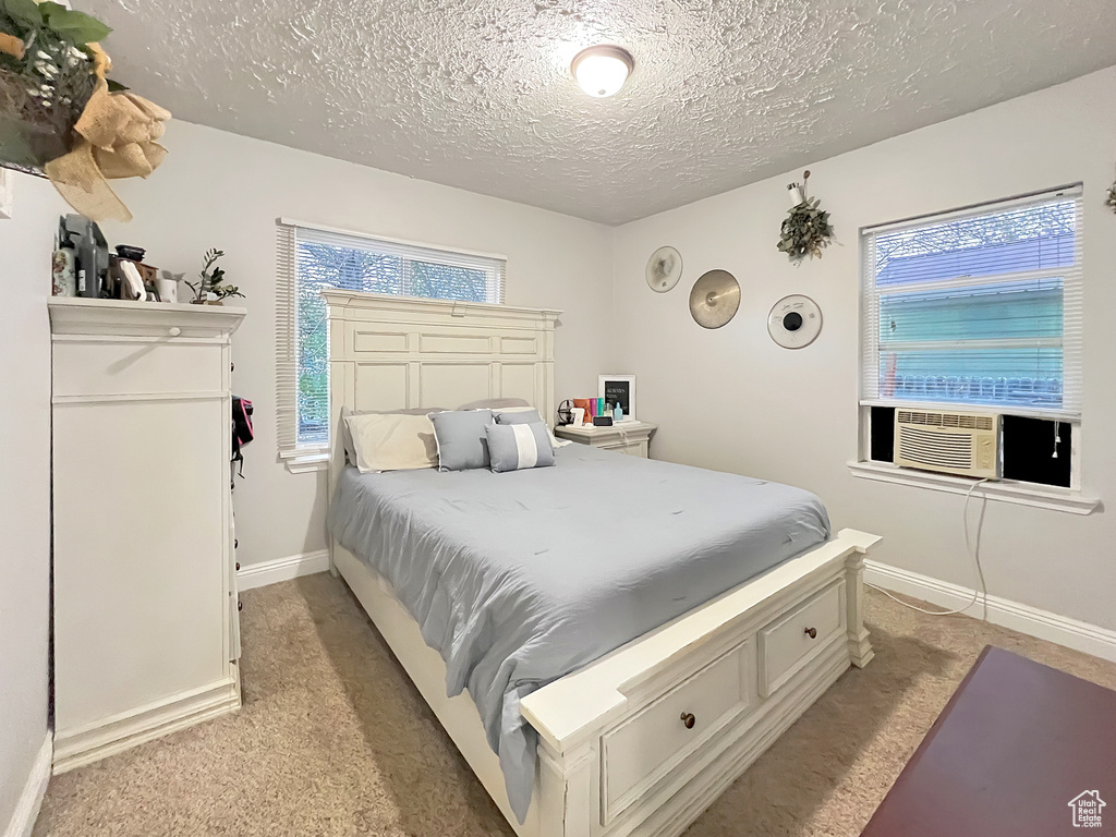 Bedroom featuring baseboards, a textured ceiling, cooling unit, and light carpet