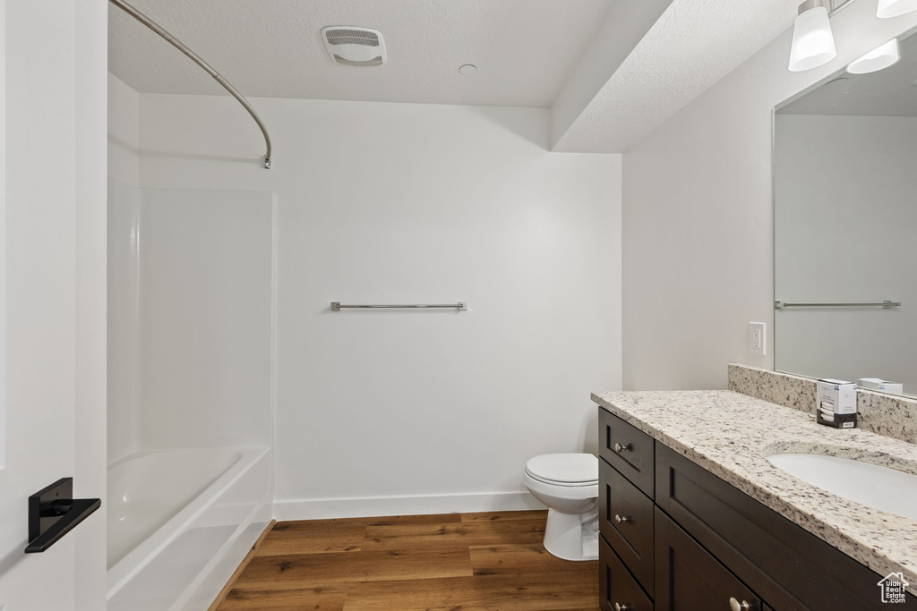 Bathroom with vanity, visible vents, shower / bathtub combination, wood finished floors, and toilet