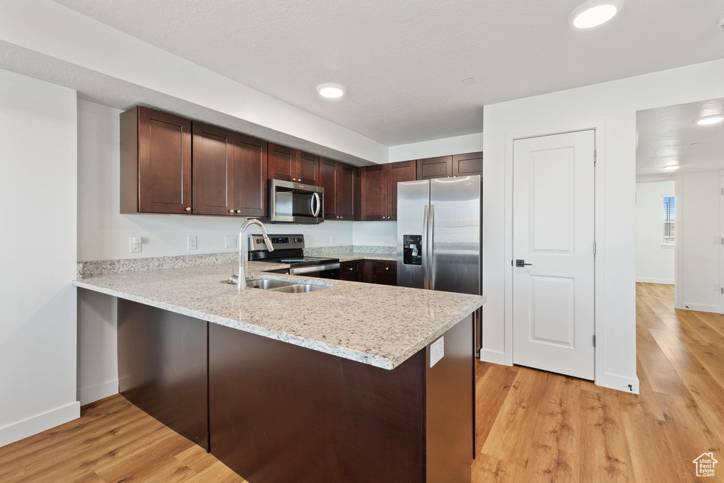 Kitchen with stainless steel appliances, light wood-style floors, a sink, and a peninsula