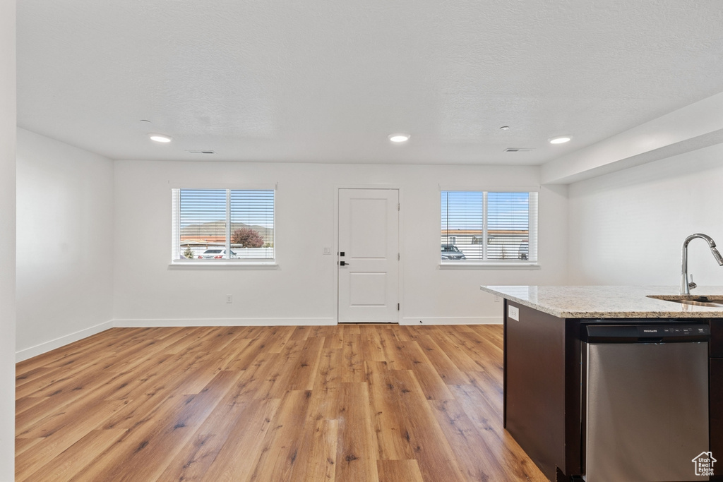 Kitchen with baseboards, light stone counters, a sink, light wood-style flooring, and dishwasher