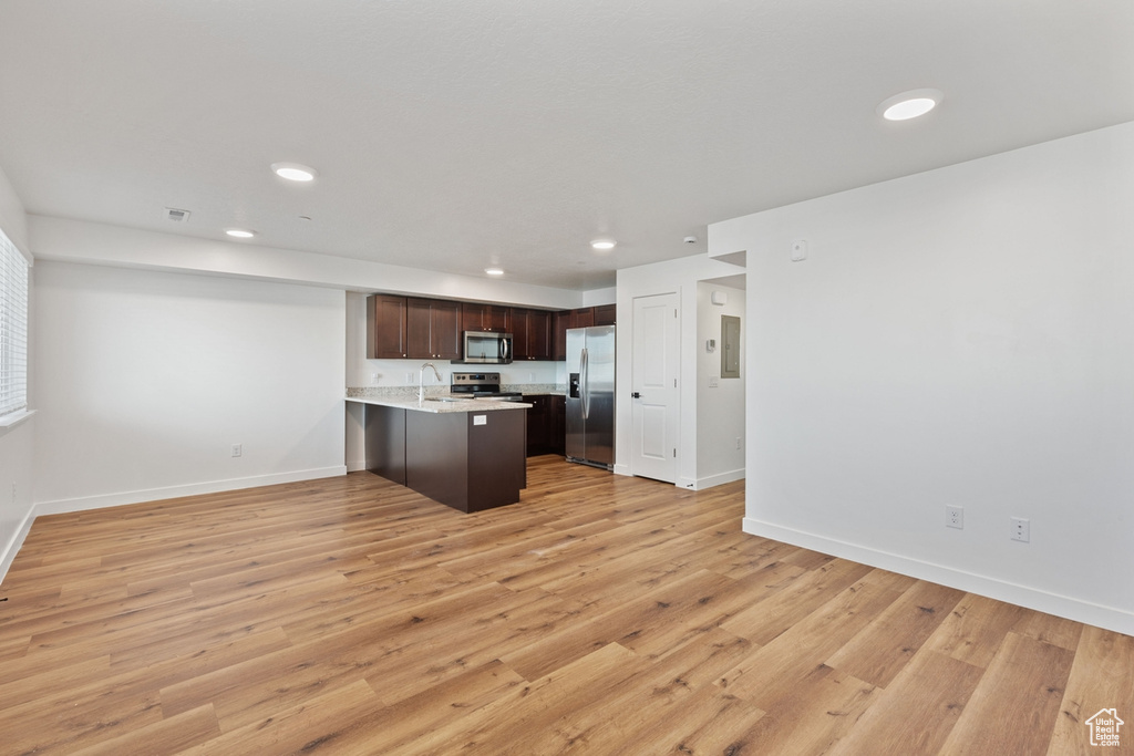 Kitchen featuring a peninsula, dark brown cabinets, open floor plan, light countertops, and stainless steel appliances