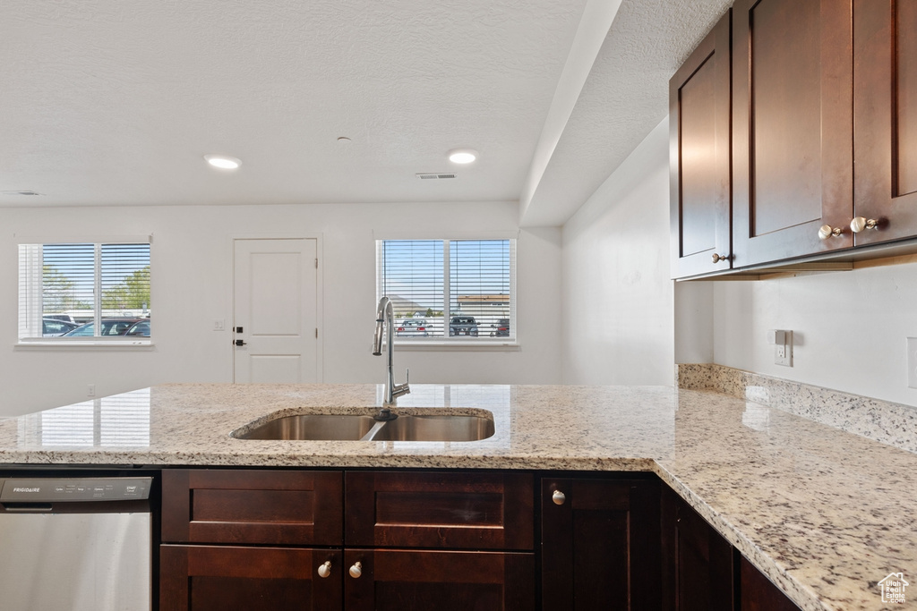 Kitchen with a sink, stainless steel dishwasher, a peninsula, and dark brown cabinets