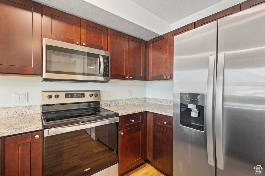 Kitchen featuring appliances with stainless steel finishes, light stone countertops, light wood finished floors, and reddish brown cabinets