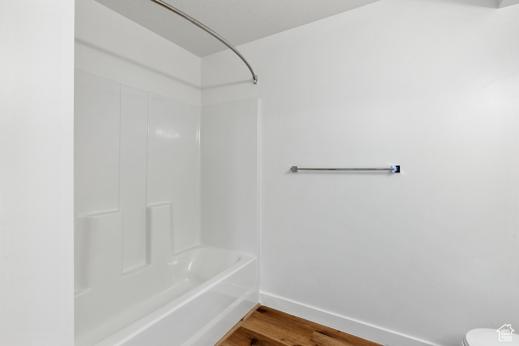 Full bathroom with baseboards, shower / bathing tub combination, toilet, and wood finished floors