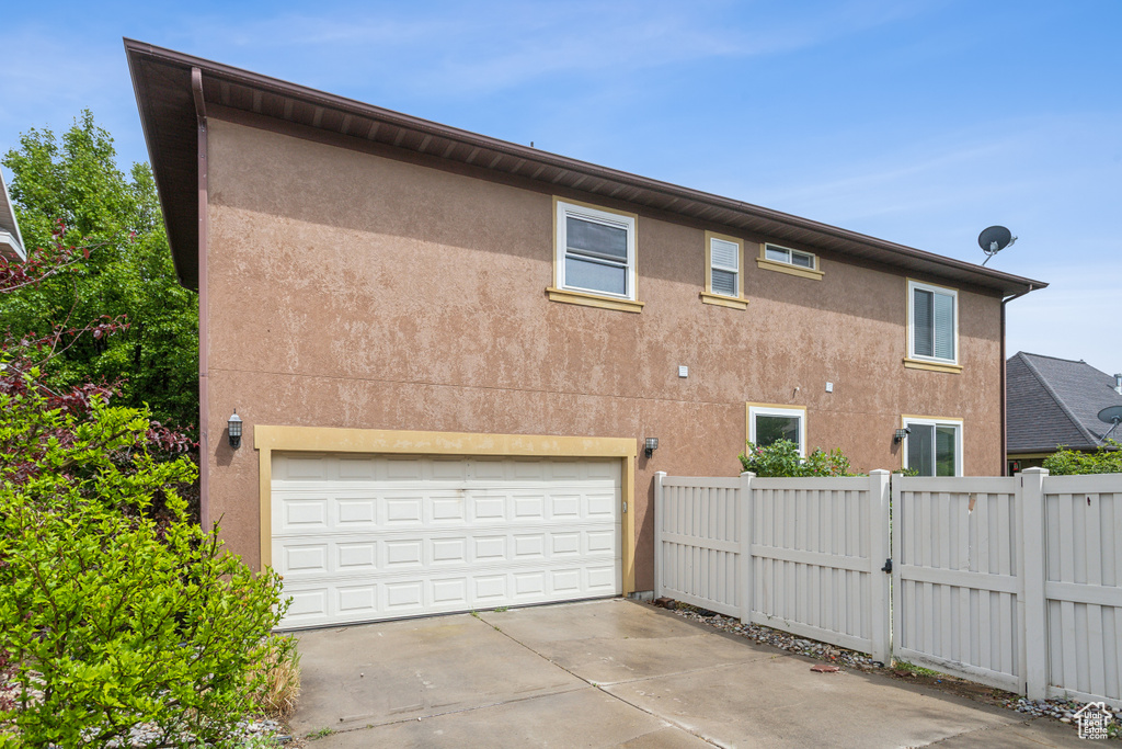 View of side of home featuring fence, concrete driveway, a garage, and stucco siding