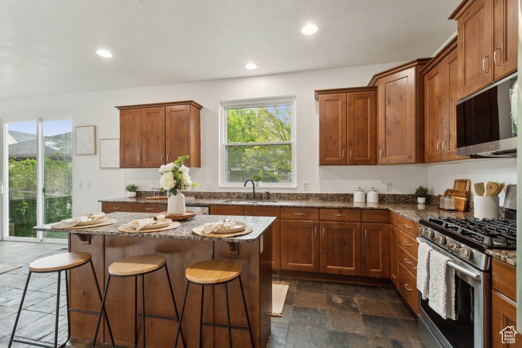 Kitchen with appliances with stainless steel finishes, stone tile flooring, a sink, a kitchen breakfast bar, and healthy amount of natural light