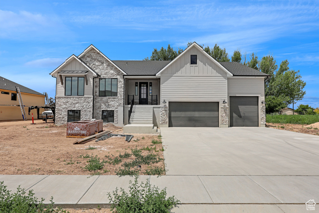 View of front facade with board and batten siding, an attached garage, driveway, and stone siding