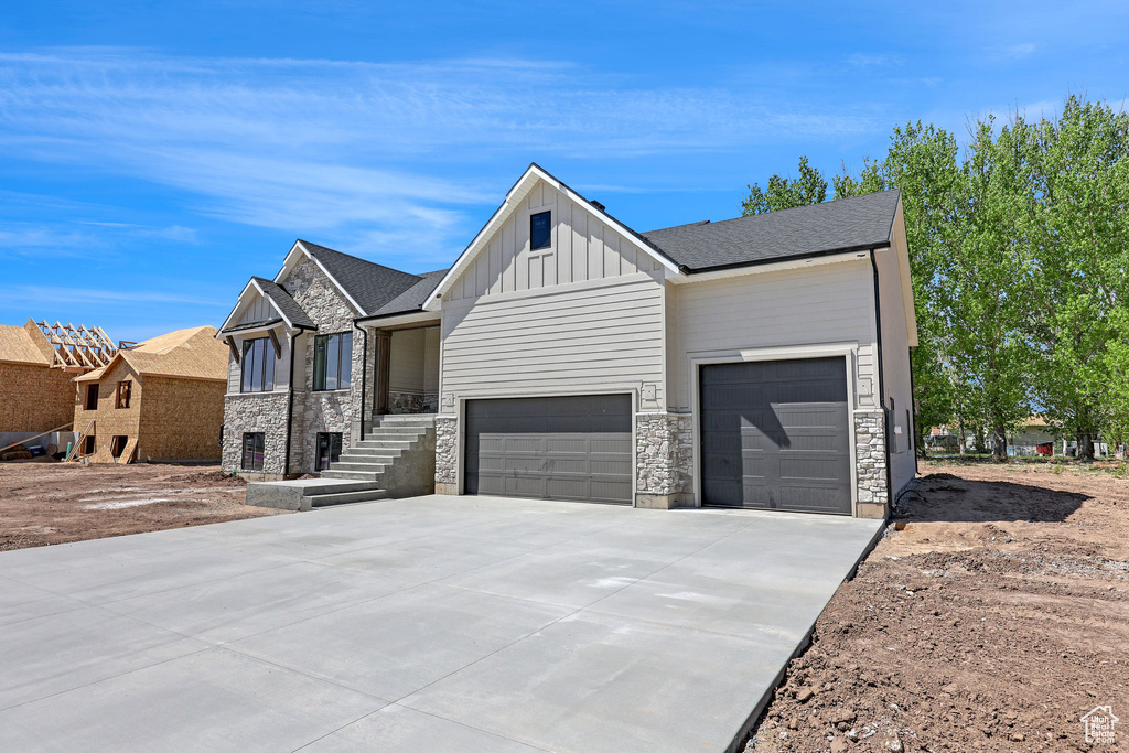View of front of property with a garage, board and batten siding, driveway, and stone siding