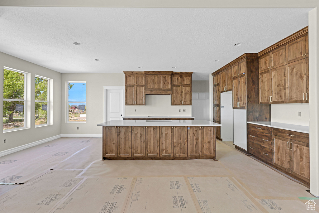 Kitchen with a kitchen island, baseboards, light countertops, a textured ceiling, and white refrigerator