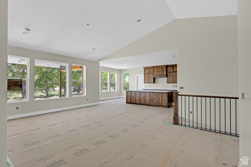 Unfurnished living room with high vaulted ceiling and baseboards
