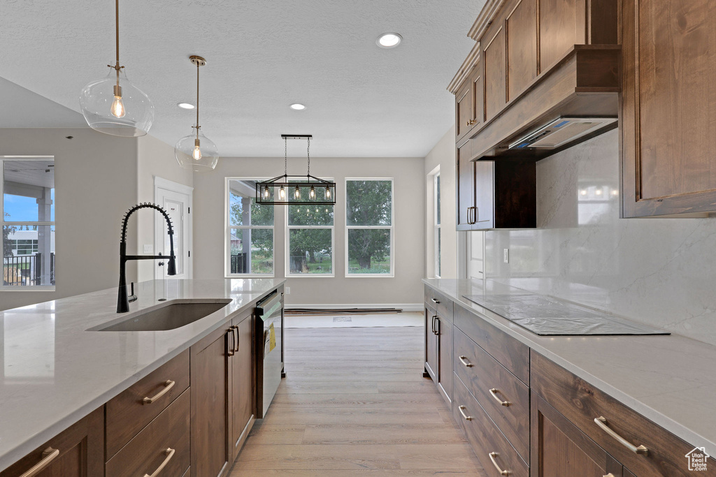 Kitchen featuring electric cooktop, stainless steel dishwasher, light wood-type flooring, pendant lighting, and light stone countertops