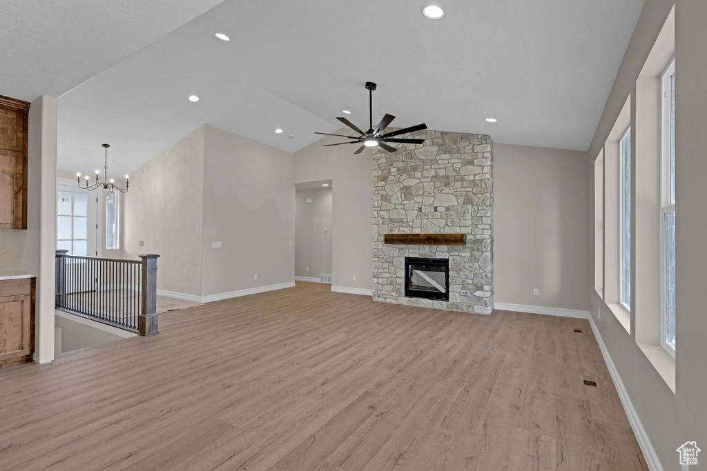 Unfurnished living room featuring light wood-style flooring, ceiling fan, vaulted ceiling, a fireplace, and a chandelier