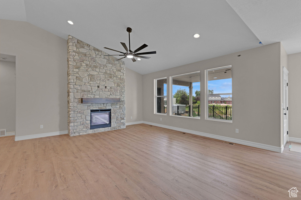Unfurnished living room with vaulted ceiling, ceiling fan, light wood finished floors, a stone fireplace, and recessed lighting