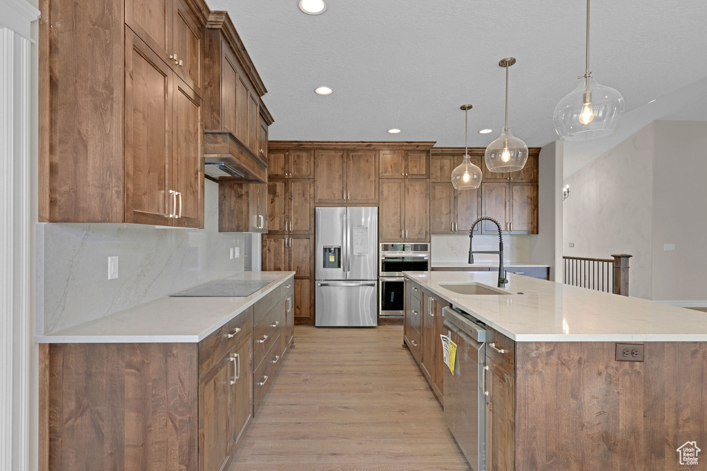 Kitchen featuring appliances with stainless steel finishes, light wood-style floors, decorative backsplash, hanging light fixtures, and recessed lighting