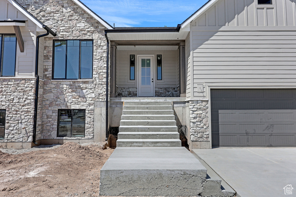 View of exterior entry featuring board and batten siding, an attached garage, concrete driveway, and stone siding