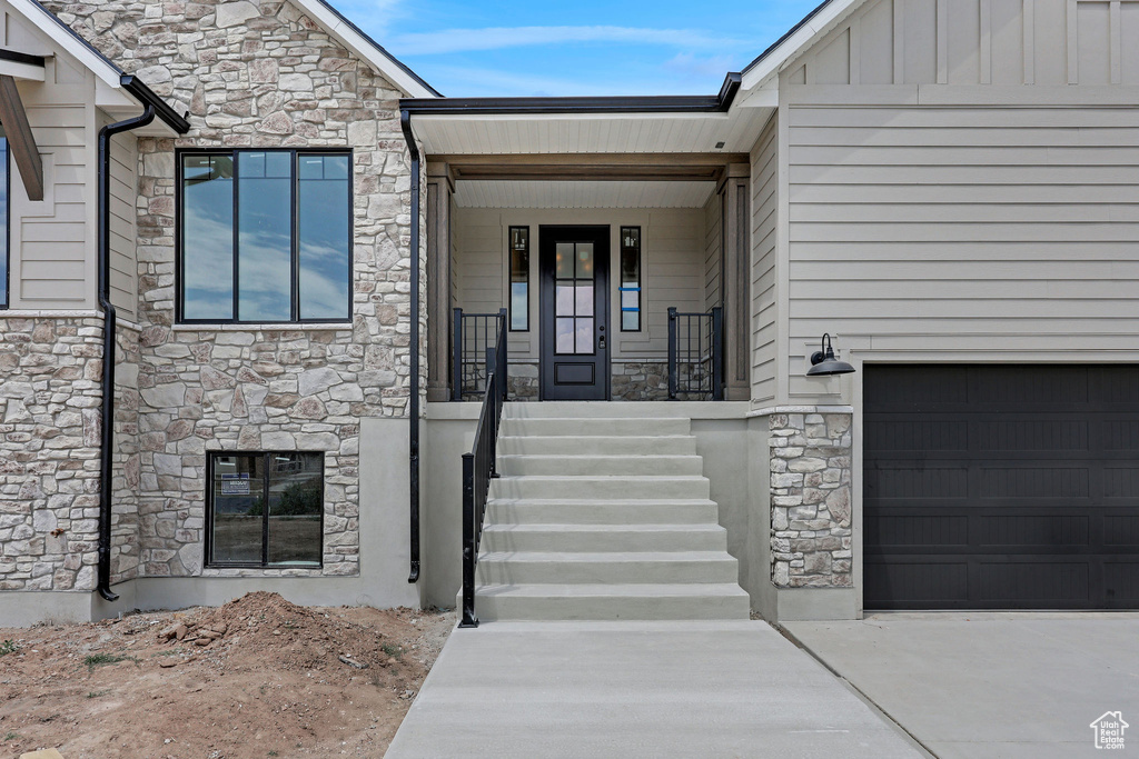 Doorway to property featuring stone siding, concrete driveway, a porch, and an attached garage
