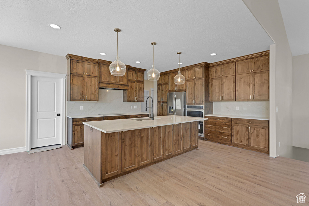 Kitchen featuring stainless steel refrigerator with ice dispenser, light wood finished floors, tasteful backsplash, a kitchen island with sink, and recessed lighting