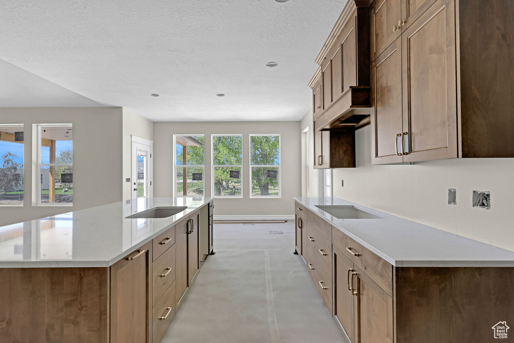 Kitchen featuring baseboards, a center island with sink, light countertops, a textured ceiling, and concrete floors