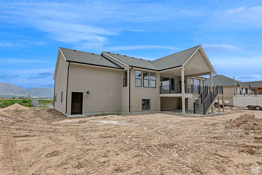 Back of property featuring stairs, a mountain view, stucco siding, and roof with shingles