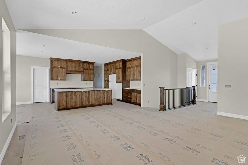 Kitchen with brown cabinetry, light countertops, baseboards, and a kitchen island
