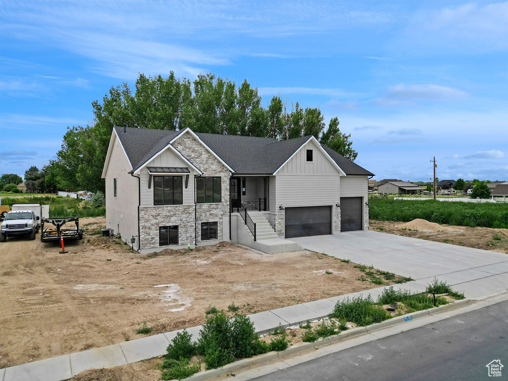 View of front of property with board and batten siding, concrete driveway, stone siding, a garage, and roof with shingles