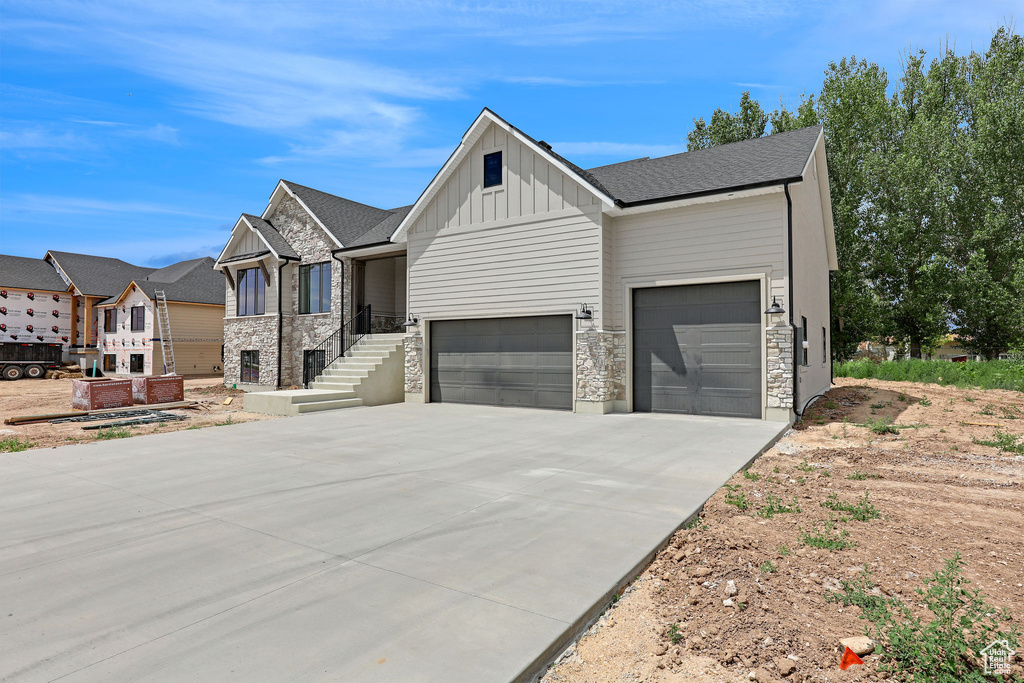 View of front of house with board and batten siding, a garage, driveway, and stone siding