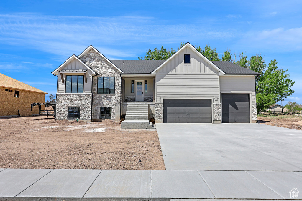 View of front facade with board and batten siding, an attached garage, driveway, and stone siding