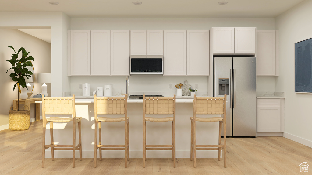 Kitchen featuring a kitchen breakfast bar, stainless steel appliances, light wood finished floors, and white cabinets