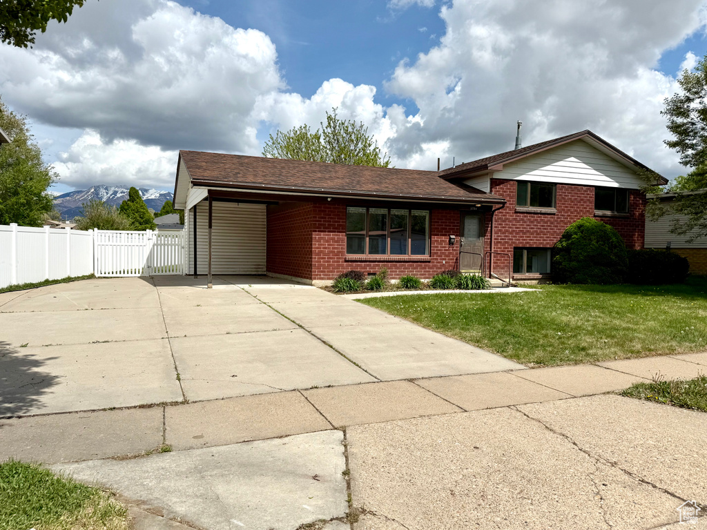 Tri-level home featuring fence, a front lawn, brick siding, a gate, and concrete driveway